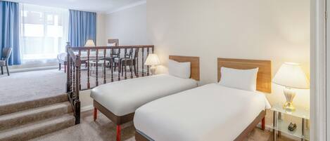 A hotel room with two beds, a staircase, a desk with a lamp, and a view of the outside.