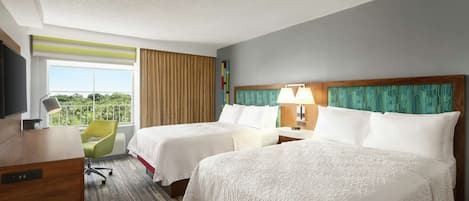 A hotel room with two beds, a desk with a TV, a chair, and a window with curtains.