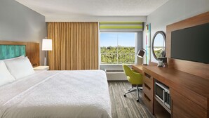 Ein Hotelzimmer mit Bett, Schreibtisch, Fernseher und Blick auf Grün durch das Fenster.