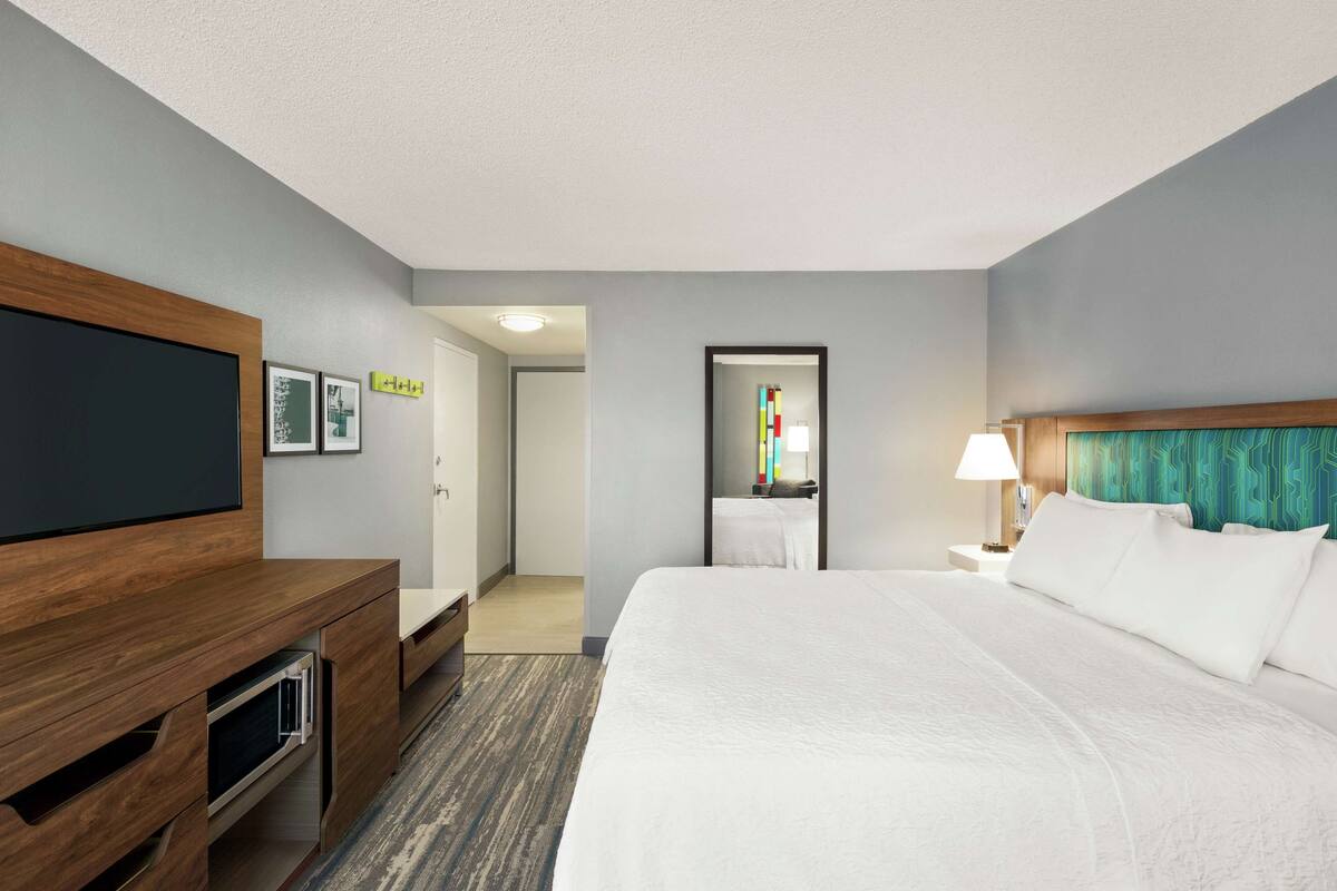 Een hotelkamer met een groot bed, een houten bureau, een flatscreen televisie en een deur naar een badkamer.