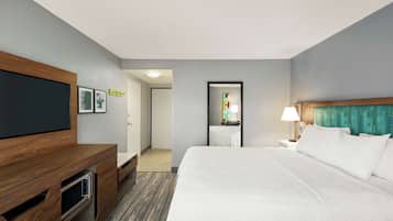 A hotel room with a large bed, a wooden desk, a flat-screen TV, and a door leading to a bathroom.