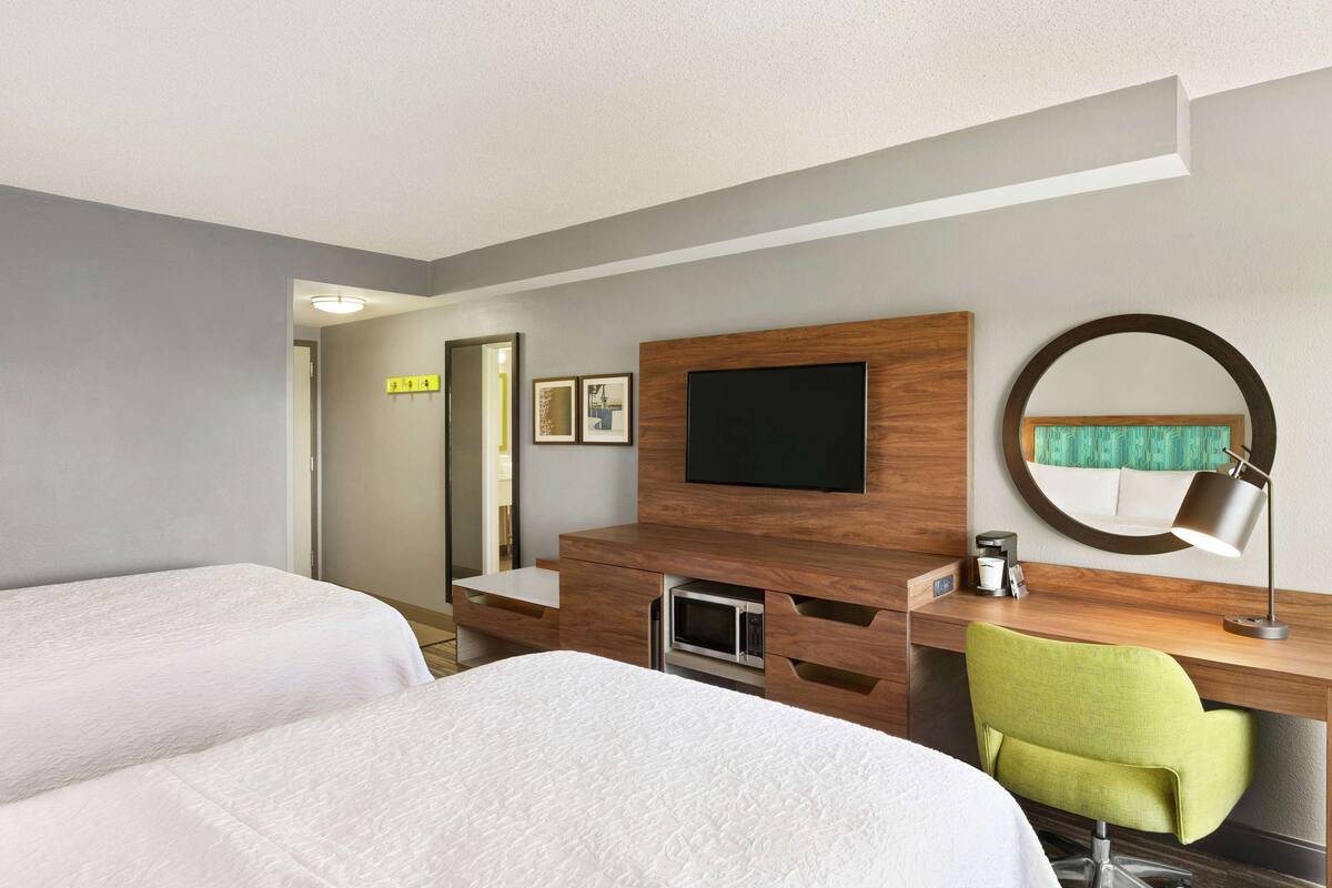 Une chambre d’hôtel avec deux lits, un bureau doté d’un téléviseur à écran plat, un micro-ondes, une lampe et un fauteuil vert.