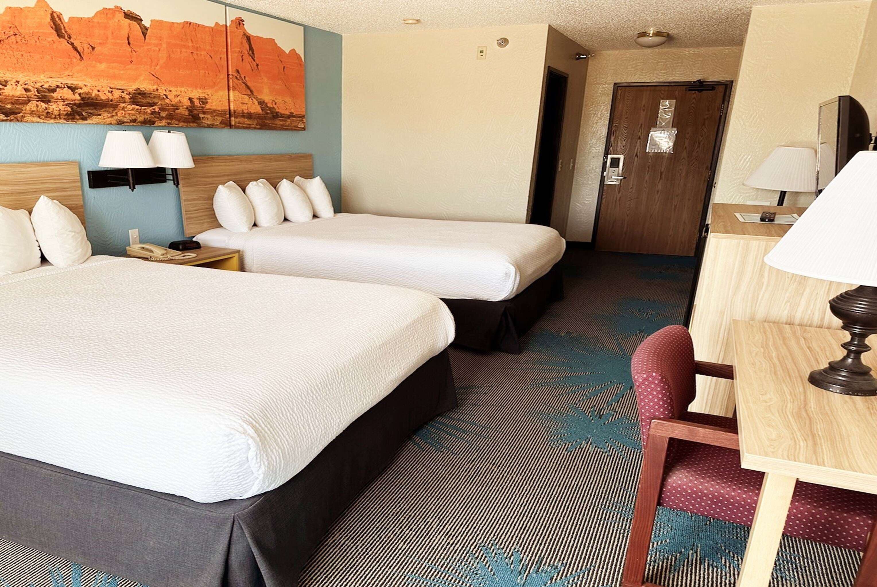 A hotel room with two beds, a desk, a chair, a telephone, and a wall-mounted lamp.