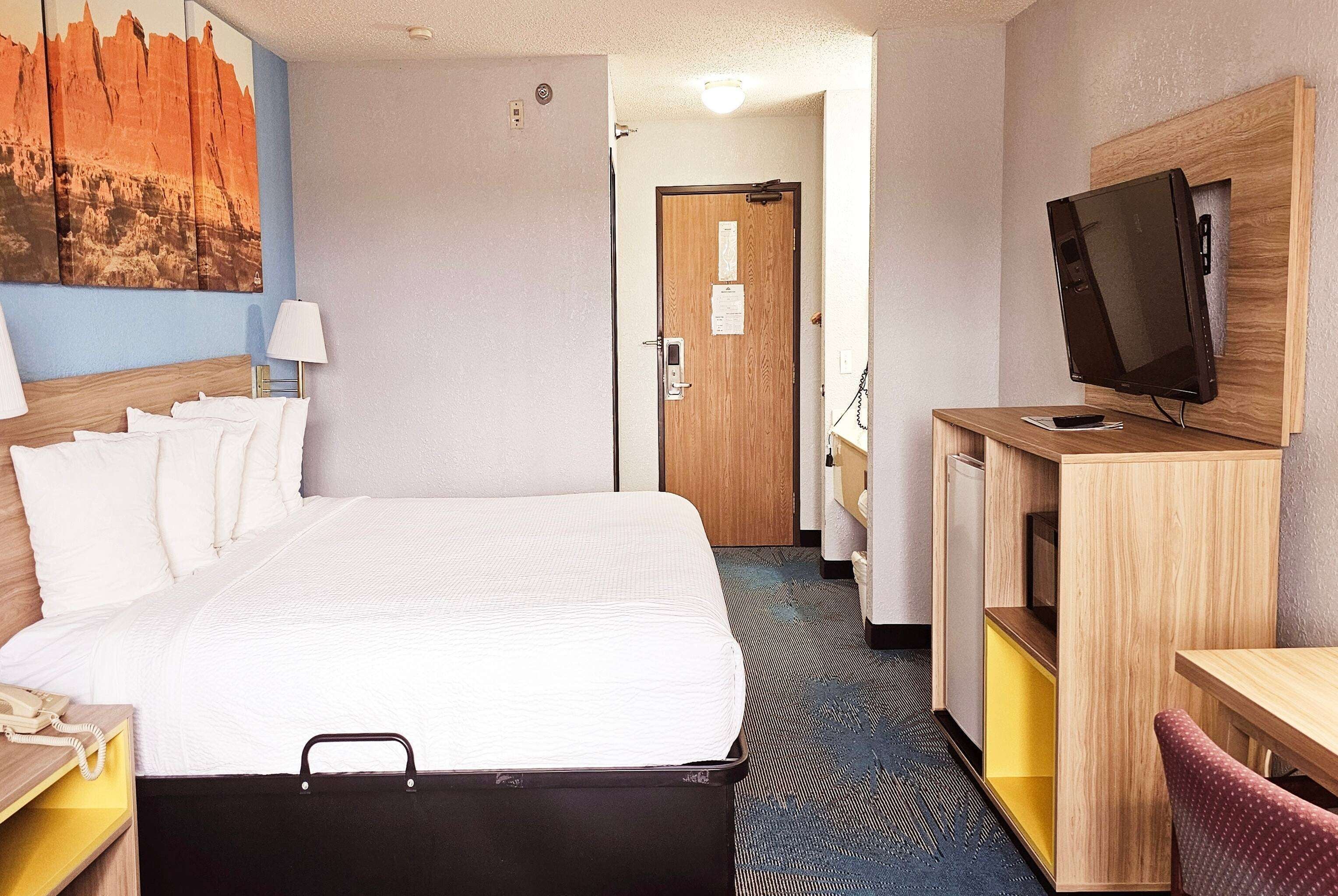 A hotel room with a bed, a desk with a computer, a TV, and a door leading to another room.