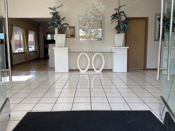 A reception area with a tiled floor, two potted plants, a reception desk, and a large mirror on the wall.