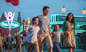 A family walking with balloons in front of a neon sign.