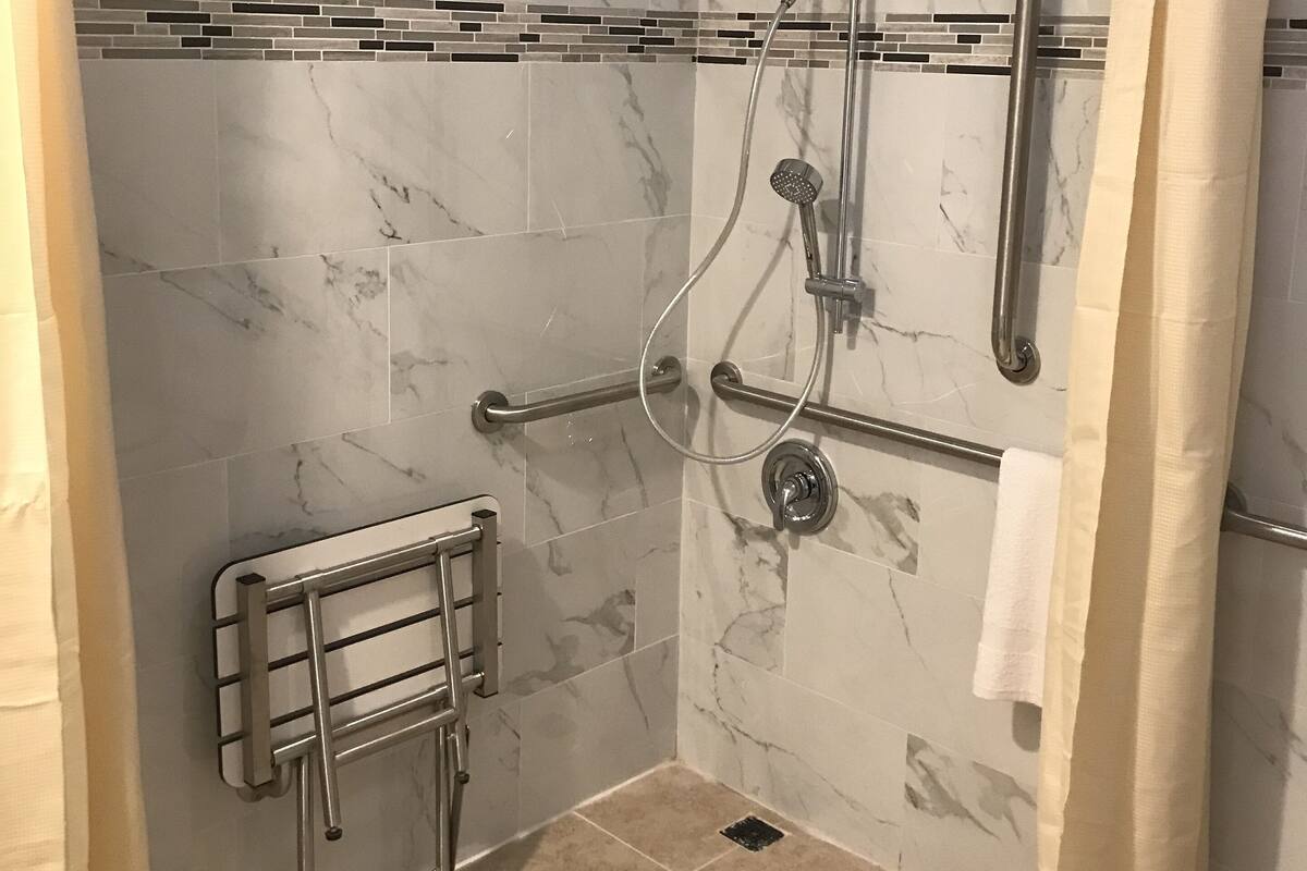 A shower area with a glass door, a handrail, a towel rack, and a tiled floor.