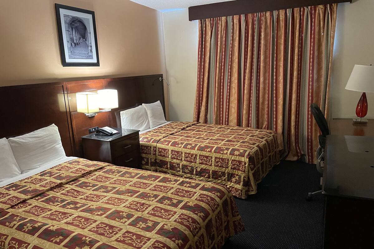 A hotel room with two beds, a nightstand, a lamp, and a framed picture on the wall.