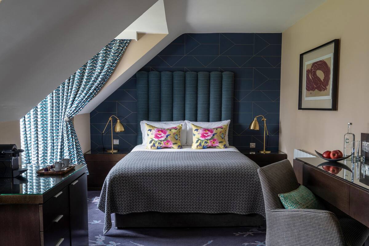 A modern bedroom with a large bed, a desk, and a chair. There is a staircase leading to an upper level.