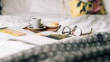 Una cama bien hecha con una taza de café, un plato de comida y un par de gafas sobre una bandeja.