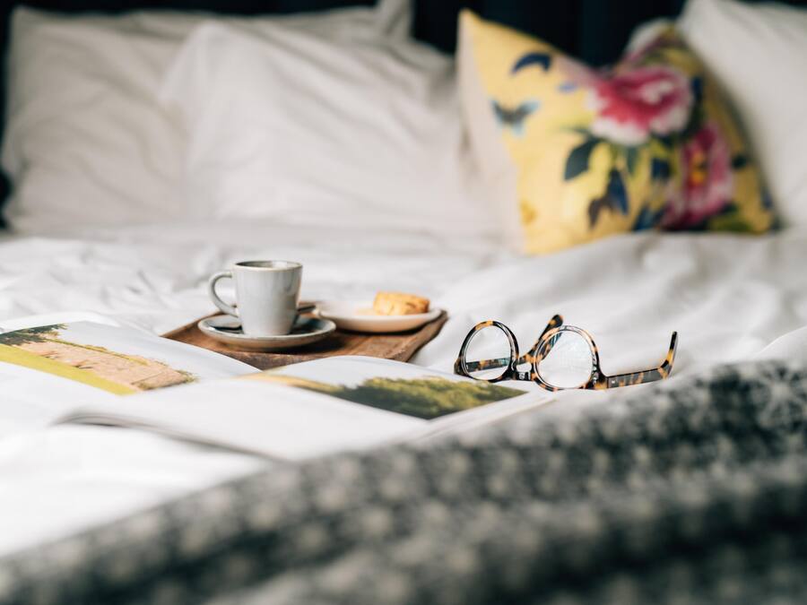 Un lit bien fait, avec une tasse de café, une assiette de nourriture et une paire de lunettes posées sur un plateau.