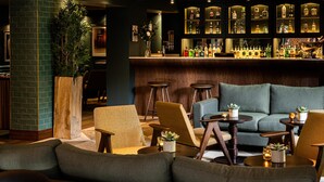 En bar med et udvalg af spiritusflasker, en siddeplads med sofaer og stole, og en stor plantepotte.