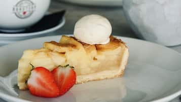 Een nagerechtenbord met een plakje taart, belegd met een bolletje ijs en een aardbei, een kop koffie en een schaal fruit.
