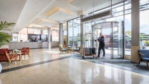 Et hotel lobby med en drejeindgang, en receptionsdisk og et siddeområde med stole og borde.