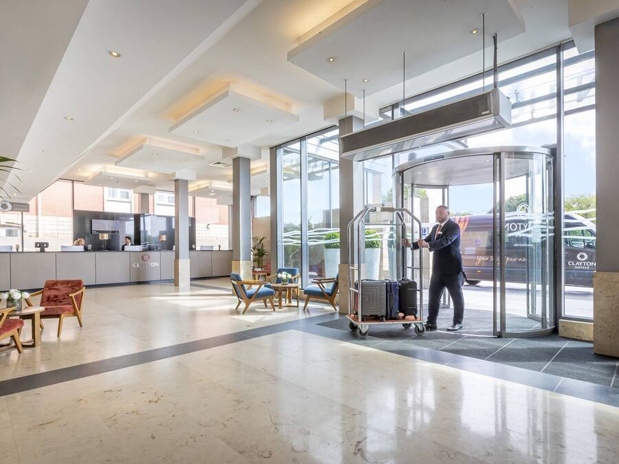 Un hall d’hôtel doté d’une porte tournante, d’un comptoir d’accueil et d’un espace détente avec des chaises et des tables.