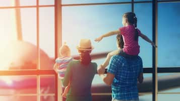 A family of three at an airport, with a child on the shoulders of an adult.