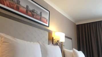 A hotel room with a bed, pillows, a headboard, a wall-mounted lamp, and a framed picture.