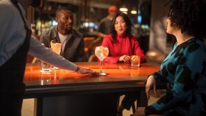 En bar med en bartender der serverer drikkevarer til gæster ved et bord.