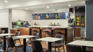 A modern restaurant with multiple tables and chairs, a counter with a menu board, and a coffee machine. - Courtyard by Marriott Gainesville FL (Gainesville)