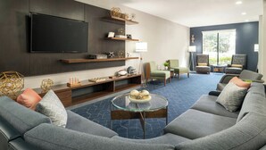 A modern living room with a large flat-screen TV, built-in shelves, a glass coffee table, and a seating area with sofas and chairs. - Courtyard by Marriott Gainesville FL (Gainesville)