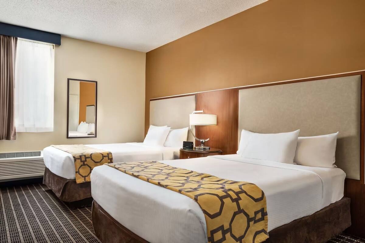 Une chambre d’hôtel avec deux lits, un grand miroir, une lampe de chevet et une fenêtre avec des rideaux.