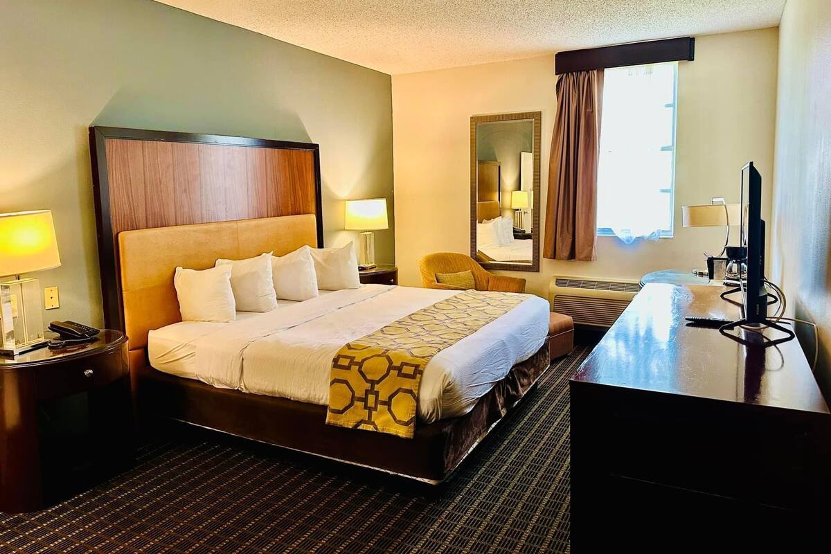 Une chambre d’hôtel avec un grand lit, des lampes de chevet, un bureau avec un ordinateur et une fenêtre avec des rideaux.