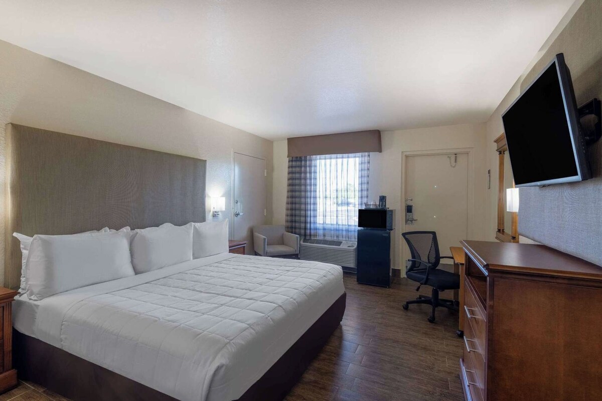 A hotel room with a large bed, a desk, a chair, a television, and a window with curtains.