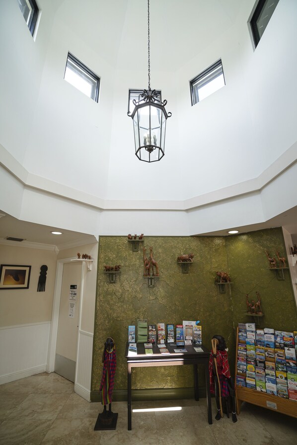 A lobby with a high ceiling, a chandelier, a reception desk, and a display of informational brochures. - Staywell Hotel (Florida City)