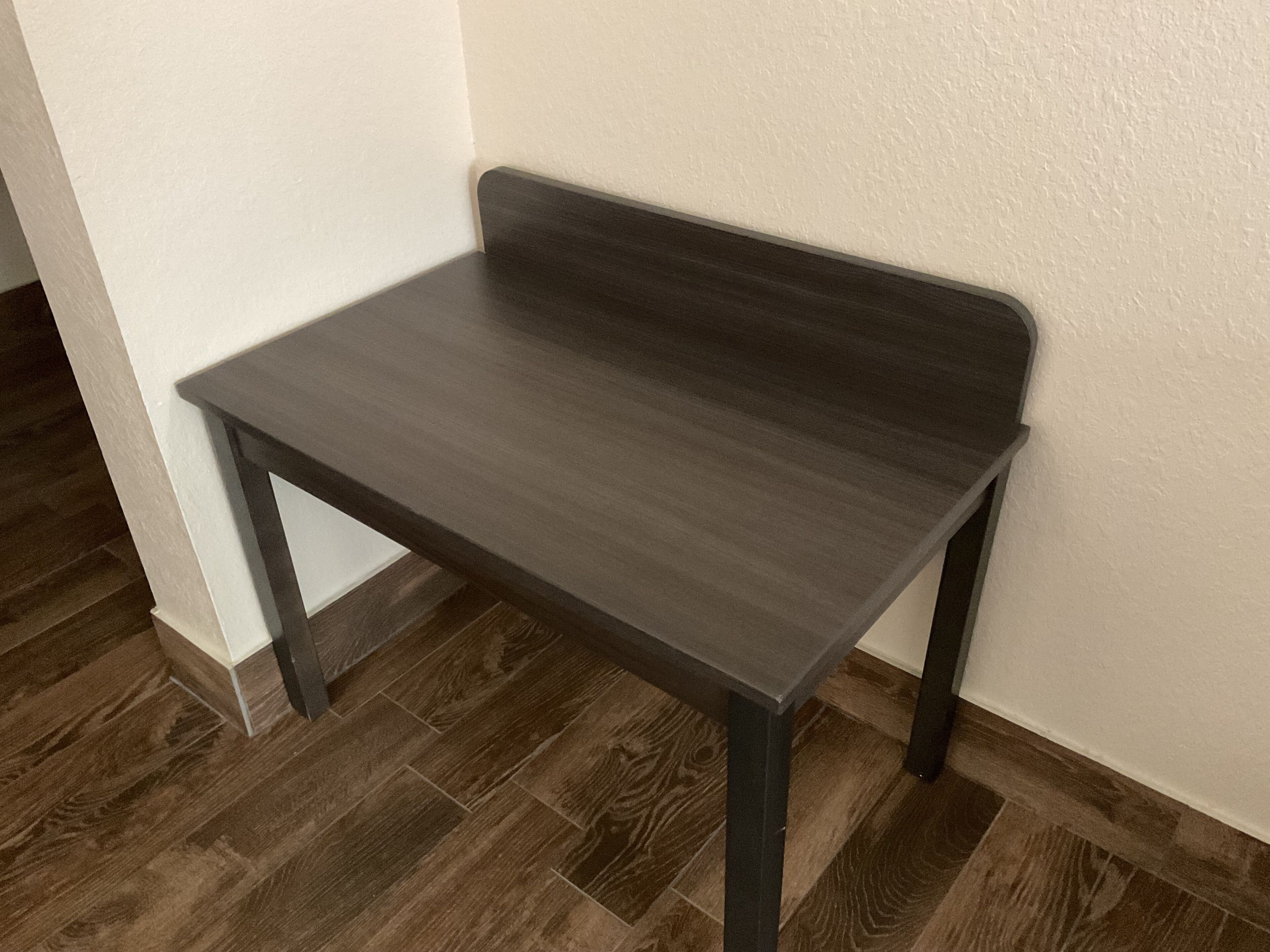 Una mesa de madera oscura de diseño sencillo, ubicada frente a una pared blanca con suelo de madera.