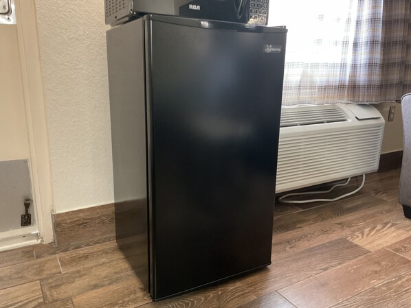 A black refrigerator in a room with wooden flooring and a white air conditioning unit.