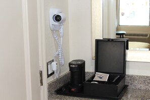 A hotel room with a hair dryer mounted on the wall, a coffee maker, and a tray with a card and a pen. - Staywell Hotel (Florida City)