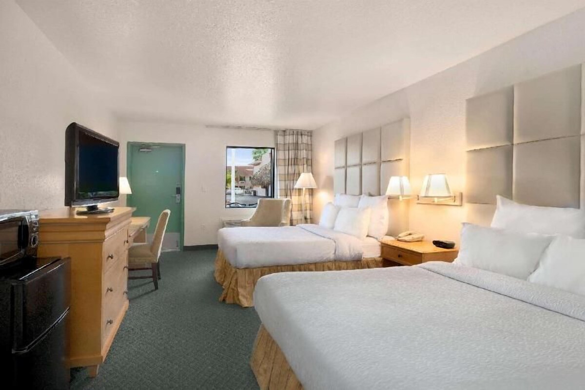 A hotel room with two beds, a desk with a television, a chair, and a window with a view.