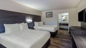 Habitación de hotel con dos camas, un televisor, un escritorio y un baño visible a través de una puerta abierta.