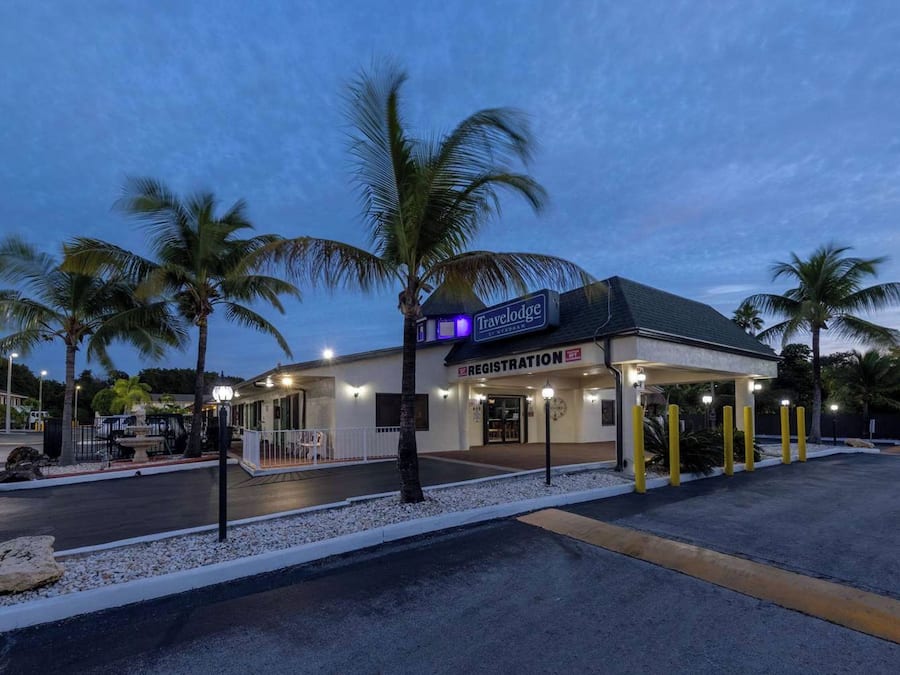 Un hotel Travelodge con una recepción, palmeras y un estacionamiento.