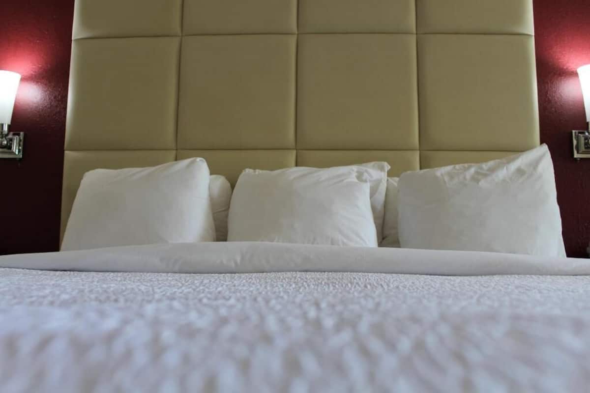 A bed with a headboard, pillows, and a wall-mounted light fixture.