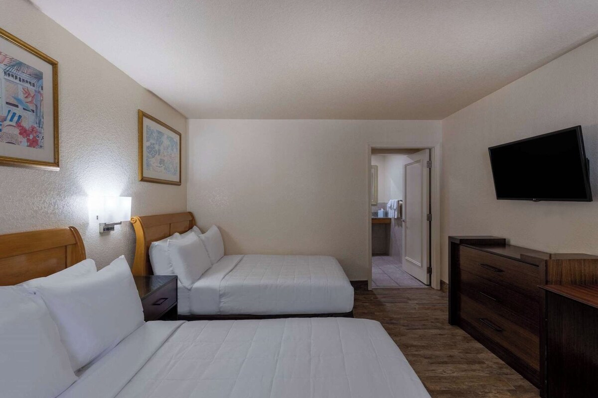 A hotel room with two beds, a TV, a dresser, and a bathroom visible through an open door.