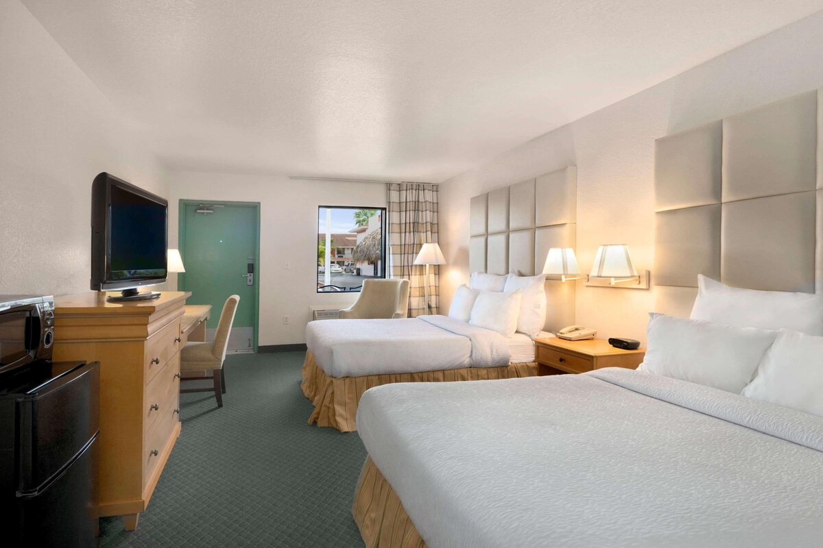 A hotel room with two beds, a TV, a desk with a lamp, and a view of the outside.