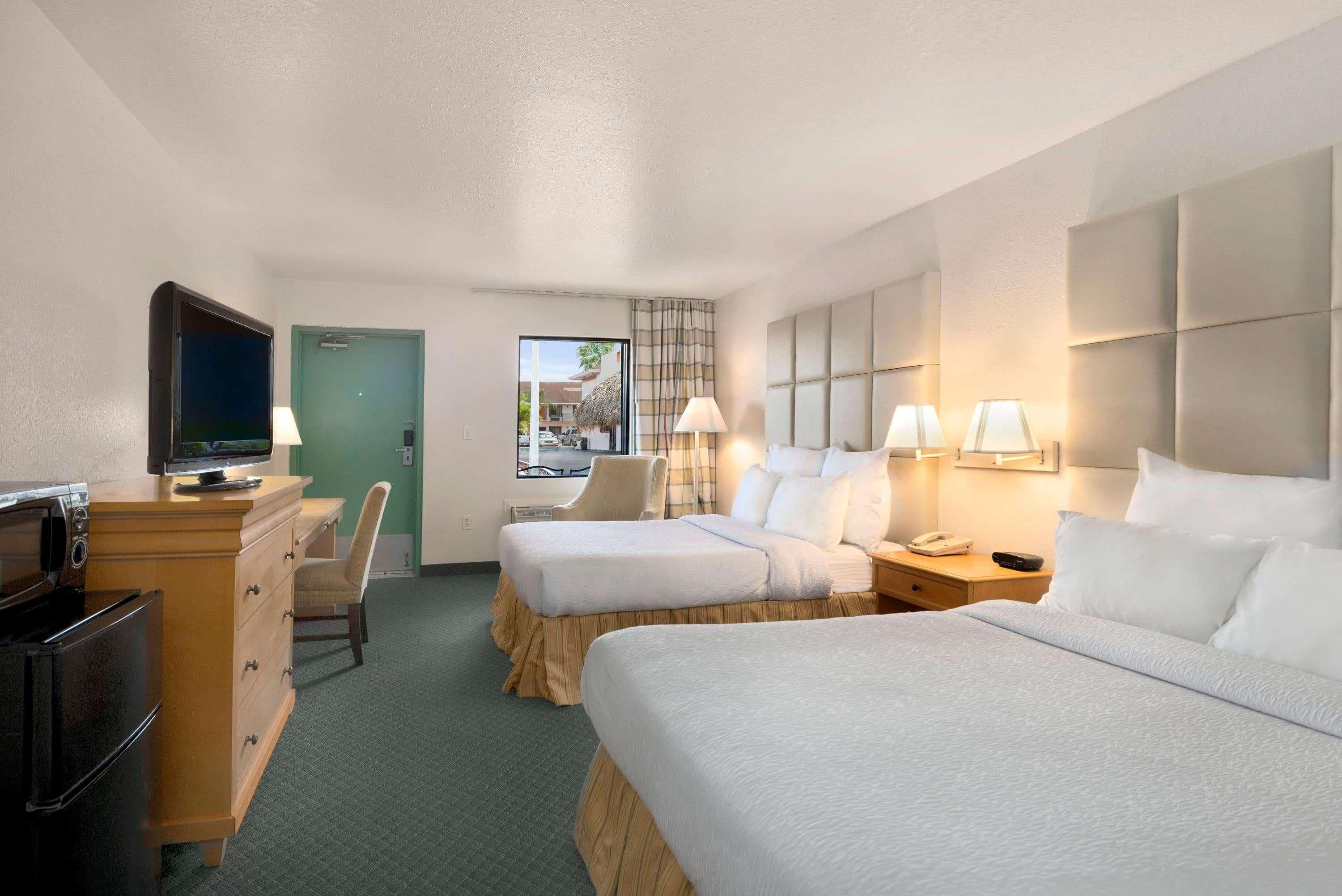 Une chambre d’hôtel avec deux lits, une télévision, un bureau avec une lampe et une vue sur l’extérieur.