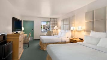 A hotel room with two beds, a TV, a desk with a lamp, and a view of the outside.