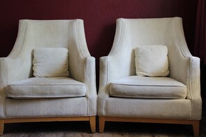 Two armchairs with cushions against a maroon wall. - Staywell Hotel (Florida City)