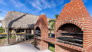 Zona de barbacoa de ladrillo con estructura de techo de paja y mobiliario de exterior.