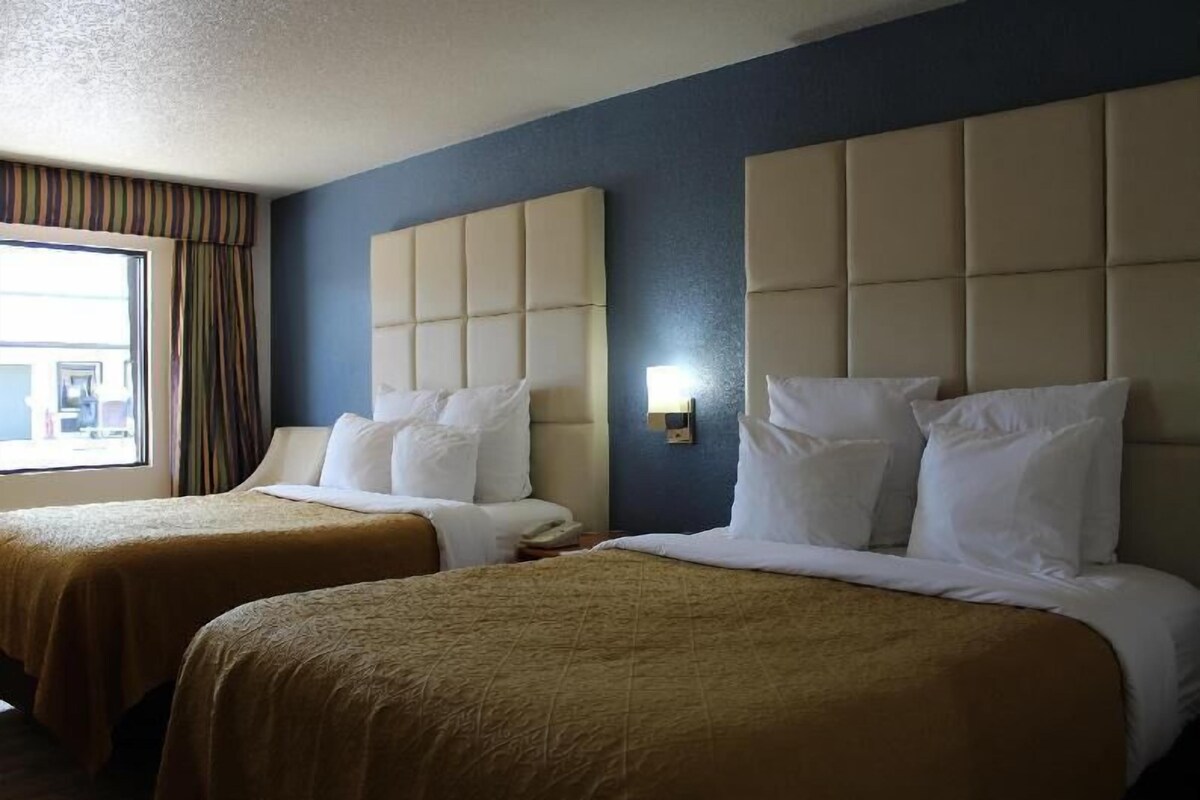 A hotel room with two beds, a window with curtains, and a wall-mounted light.