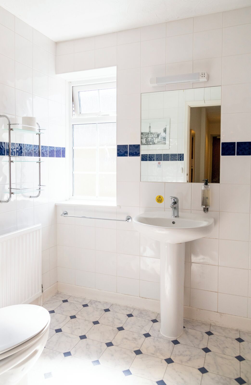 Un baño con azulejos blancos, un lavabo blanco, un espejo, una ventana y un perchero para toallas.