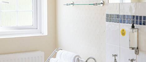 Un baño con lavabo color beige, toallero de vidrio, radiador blanco y ventana con persianas.