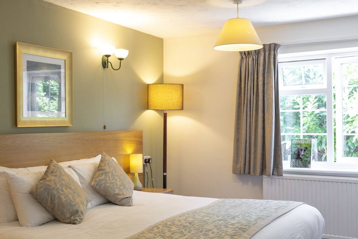 Une chambre d’hôtel avec un lit, une lampe, un tableau au mur et une fenêtre avec des rideaux.