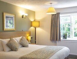 Una camera d'albergo con un letto, una lampada, un quadro appeso e una finestra con tende.