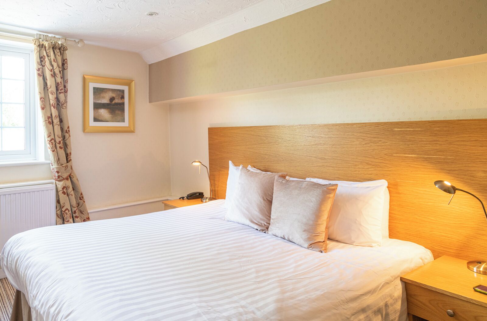 A neatly made bed with white linens, a wooden headboard, and two bedside lamps.