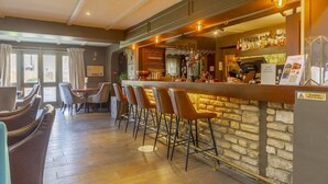 A bar area with a stone wall, bar stools, and a counter with various bottles and glasses.