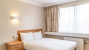 A neatly made bed with a wooden headboard, a bedside table with drawers, a wall-mounted light, and a window with curtains. - Britannia Hotel Wolverhampton (Wolverhampton)
