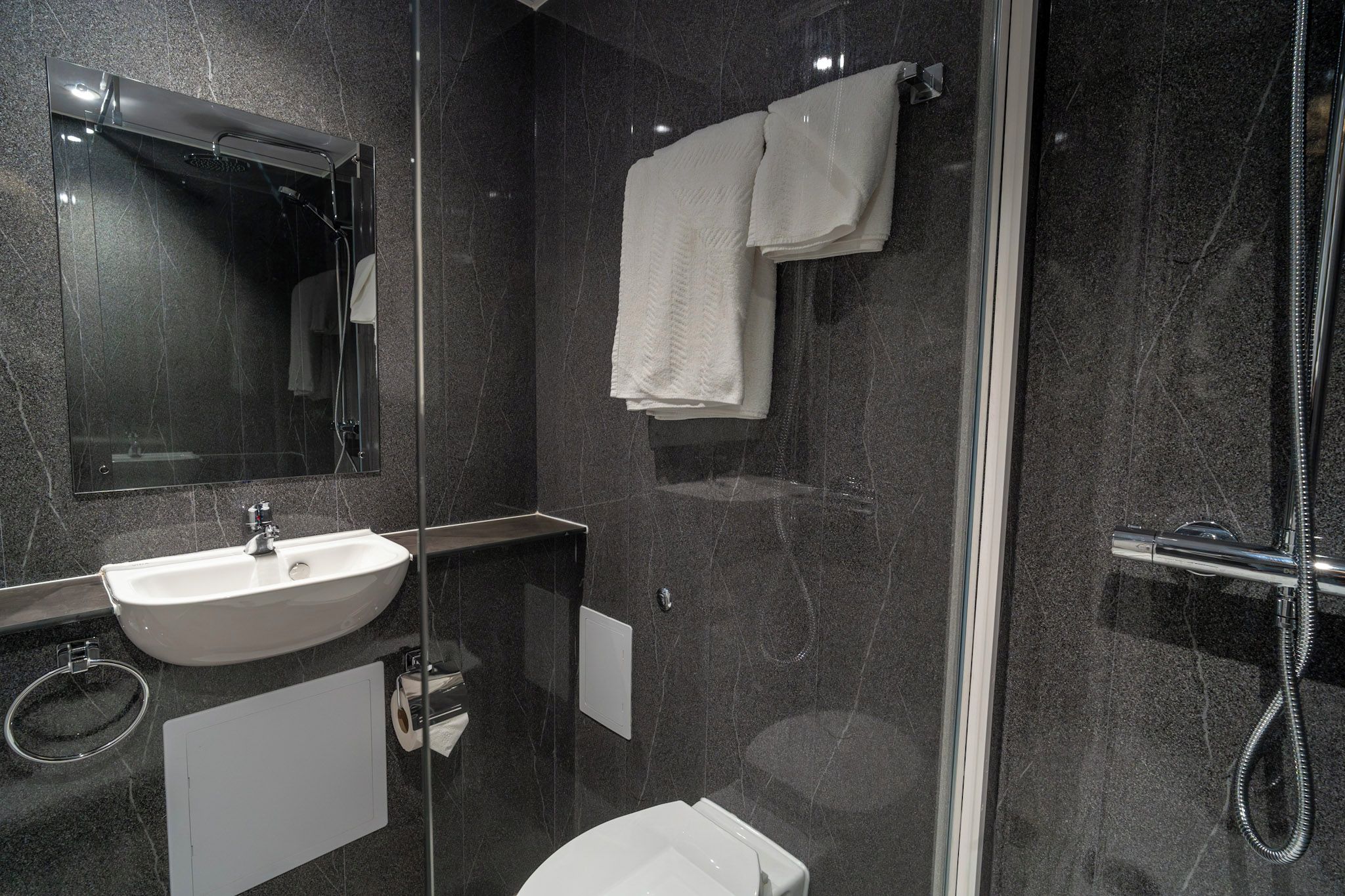 Ein modernes Badezimmer mit einer gläsernen Dusche, einem weißen Waschbecken und einem Spiegel darüber.